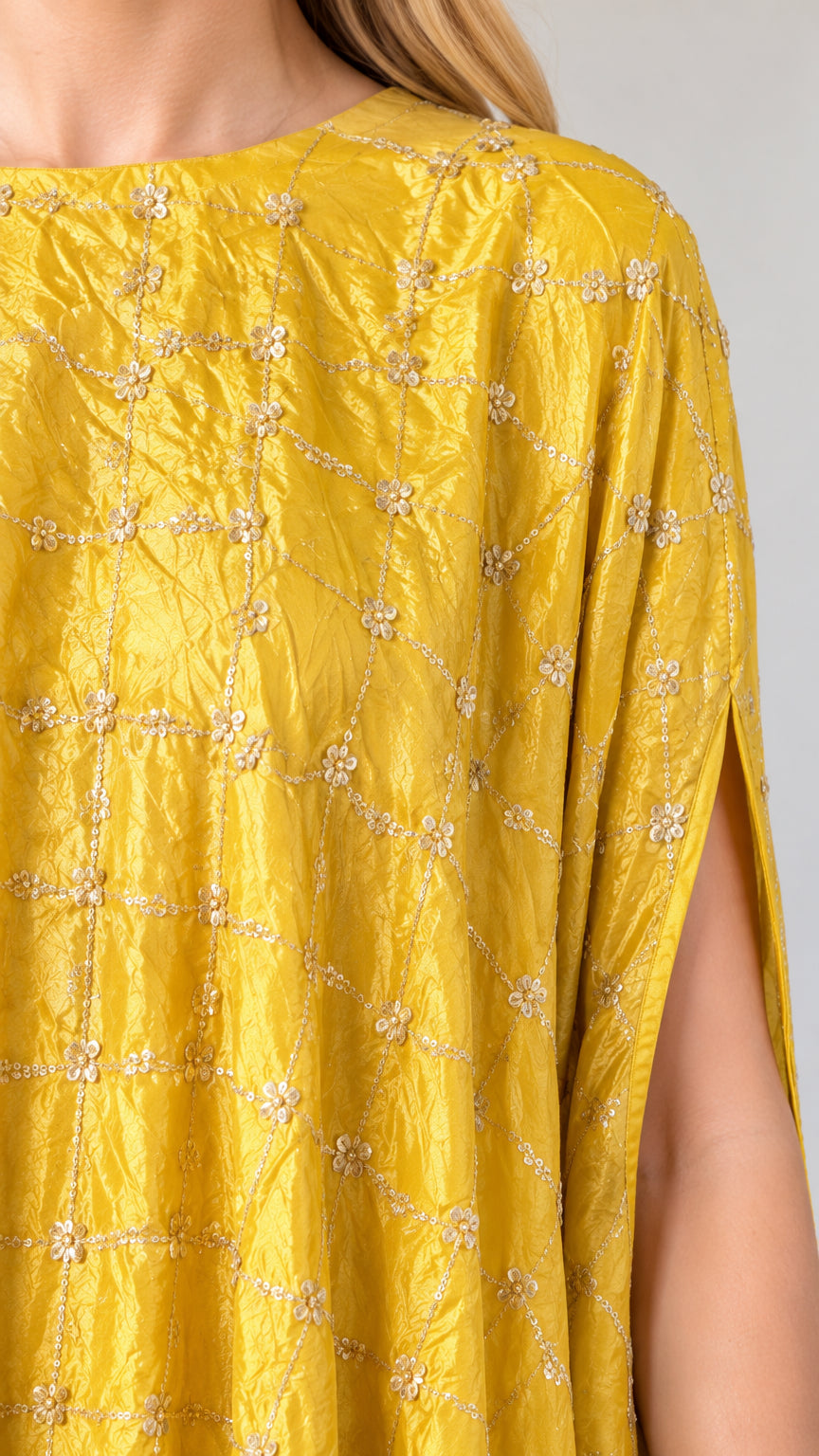 Close-up detail of textured yellow fabric with delicate embroidery and beaded fringe